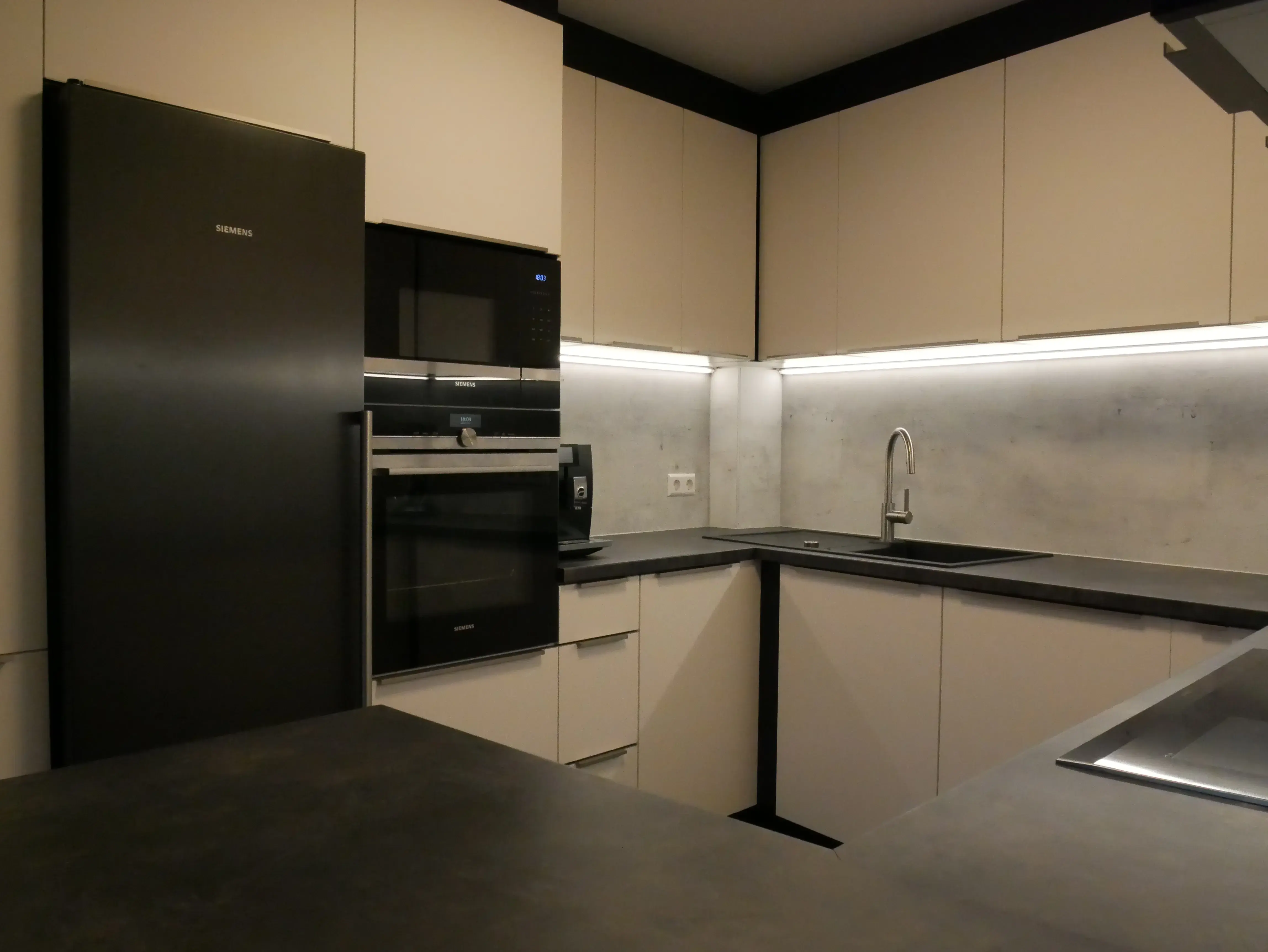 Moderne Küche mit dunklen Arbeitsplatten, weißen Schränken und Einbaugeräten.